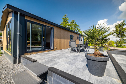 Moderne Lodge mit großer Terrasse, Gartenmöbeln und Pflanze im Vakantiepark Bergumermeer, Niederlande.