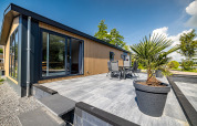 Moderne lodge med stor terrasse og havemøbler på Vakantiepark Bergumermeer i Holland, set på en solrig dag.