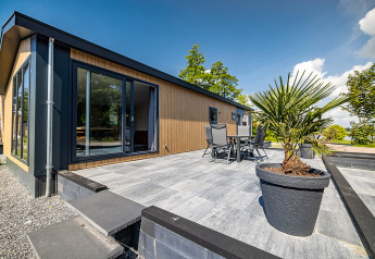 Moderne lodge med stor terrasse og havemøbler på Vakantiepark Bergumermeer i Holland, set på en solrig dag.