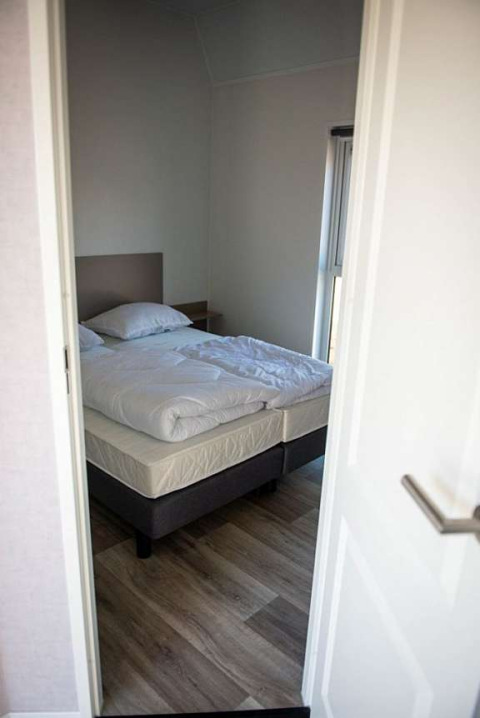 Kleines Schlafzimmer mit Doppelbett, heller Bettwäsche und Holzfußboden in Waterlodge Typ 2, Niederlande.