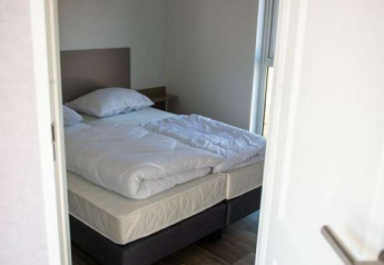 Piccola camera da letto con letto matrimoniale, biancheria bianca e pavimento in legno in Waterlodge tipo 2, Olanda.