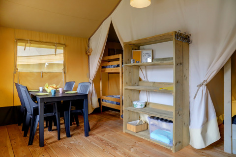 Interior of a safari tent with dining table, chairs, bunk bed, and shelves at Camping Walsheim, Germany.
