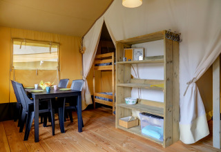 Innenansicht eines Safari-Zeltes mit Esstisch, Stühlen, Etagenbett und Regal im Camping Walsheim, Deutschland.