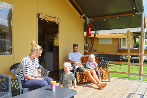 Family relaxing outside a safari tent at Camping Walsheim in Germany, sitting on a wooden deck.