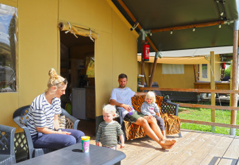 Family relaxing outside a safari tent at Camping Walsheim in Germany, sitting on a wooden deck.