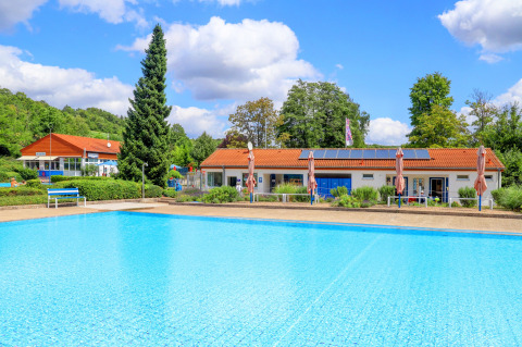 Piscina al aire libre y alojamientos de Camping Walsheim en Saarland, Alemania, rodeados de vegetación.