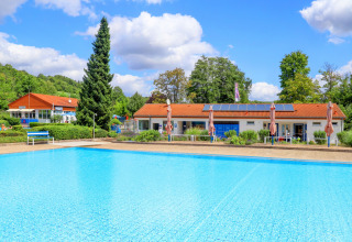 Outdoor swimming pool and holiday lodges at Camping Walsheim in Saarland, Germany, surrounded by greenery.