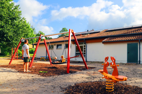 Playground with swings and spring seesaw at Camping Walsheim holiday park in Saarland, Germany, on a sunny day.