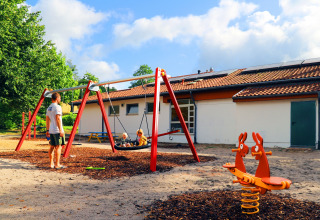Playground with swings and spring seesaw at Camping Walsheim holiday park in Saarland, Germany, on a sunny day.