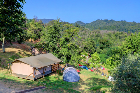 Zona de acampada en Camping Pian D'Amora, parque vacacional en la Toscana, Italia, con tiendas y colinas verdes.