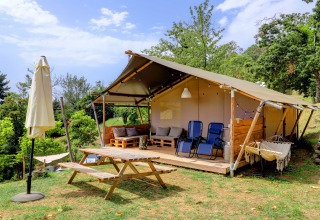 Glamping tent with wooden terrace, outdoor seating and hammock at Camping Pian D'Amora in Tuscany, Italy.