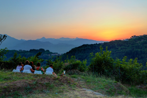 A group of people sit outdoors watching the sunset over the hills at Camping Pian D'Amora in Tuscany, Italy.