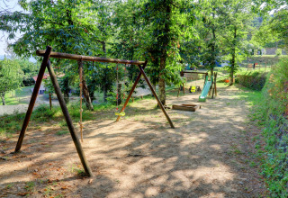 Playground at Camping Pian D'Amora in Tuscany, Italy, with swings and a slide surrounded by trees.