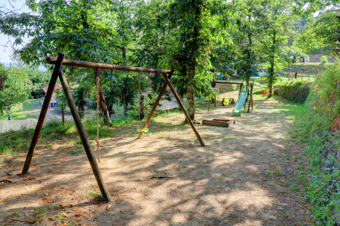 Speeltuin bij Camping Pian D'Amora in Toscane, Italië, met schommels en glijbaan tussen bomen.