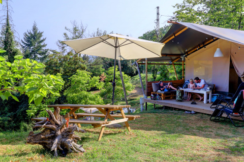 Familia relajándose en una tienda glamping en Camping Pian D'Amora, rodeada de vegetación en Toscana, Italia.