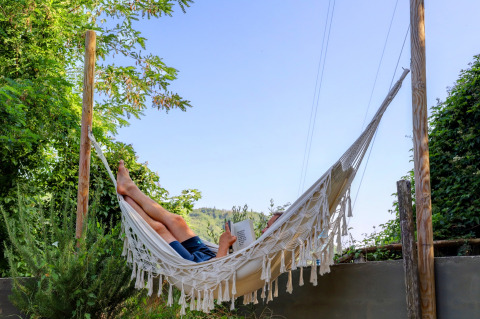Persona che si rilassa su un'amaca leggendo un libro all'aperto al Camping Pian D'Amora, Toscana, Italia.