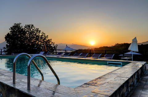 Piscina al atardecer en el Camping Pian D'Amora en la Toscana, Italia, con tumbonas y paisaje montañoso al fondo.