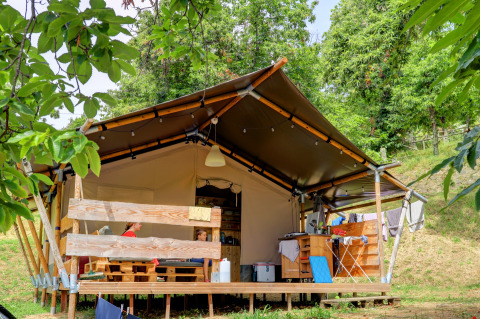 Tenda familiare al Camping Pian D'Amora in Toscana, Italia, circondata da alberi verdi e natura.