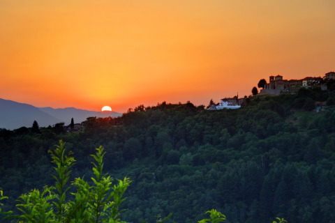 Atardecer sobre colinas boscosas y edificios en Camping Pian D'Amora, parque vacacional en la Toscana, Italia.