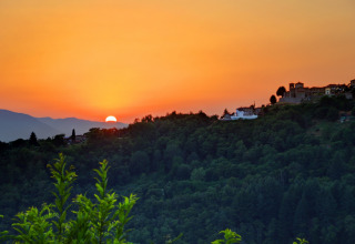 Coucher de soleil sur des collines boisées et des bâtiments au Camping Pian D'Amora en Toscane, Italie.
