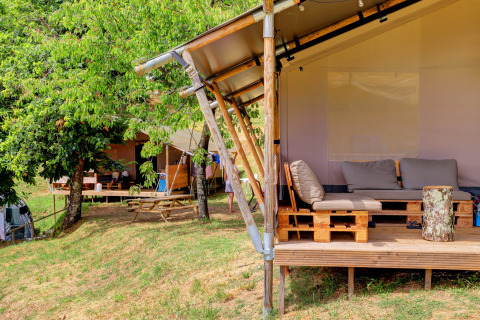 Glamping tents with outdoor seating at Camping Pian D'Amora holiday park in Tuscany, Italy, amid trees.