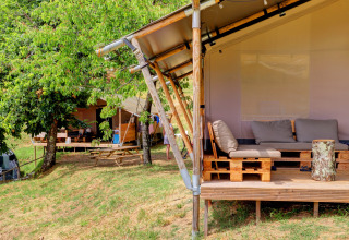 Glamping tents with outdoor seating at Camping Pian D'Amora holiday park in Tuscany, Italy, amid trees.