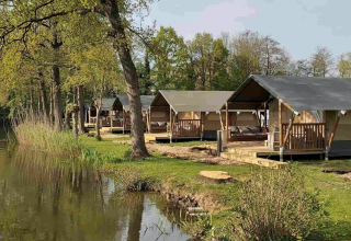 Rij glampingtenten bij het water op Camping Batenstein in Utrecht, Nederland, met bomen rondom.