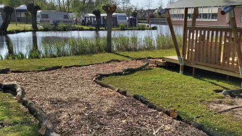 Zona de camping con caravanas y refugio de madera junto a un estanque en Camping Batenstein, Utrecht, Países Bajos.