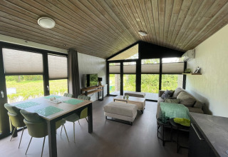Modern open-plan living room in De Parel lodge at Vakantiepark de Zeeuwse Parel, Netherlands, with large windows.