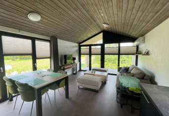 Salón moderno de planta abierta en la cabaña De Parel, Vakantiepark de Zeeuwse Parel, Países Bajos, con ventanales grandes.