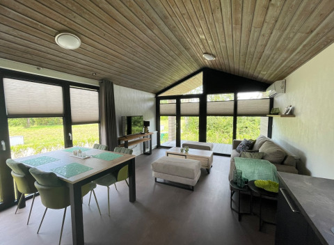Modern open-plan living room in De Parel lodge at Vakantiepark de Zeeuwse Parel, Netherlands, with large windows.