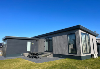 Moderne lodge ved navn De Zeester med store vinduer, græsplæne og udendørs spiseområde under blå himmel.