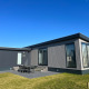 Moderne lodge ved navn De Zeester med store vinduer, græsplæne og udendørs spiseområde under blå himmel.