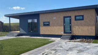 Moderne lodge ved navn Dijkzicht med træfacade og store vinduer under en blå himmel, set udefra.