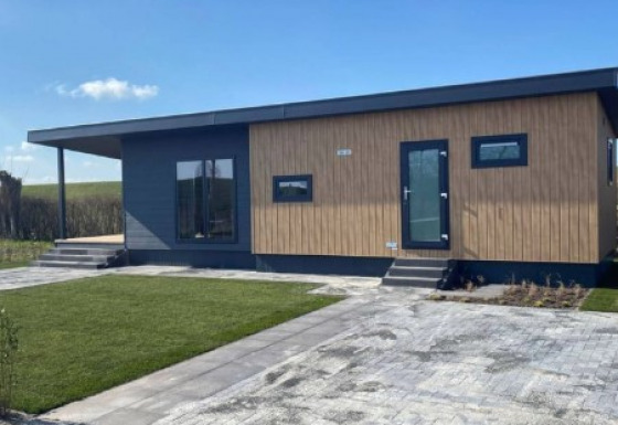 Lodge moderno llamado Dijkzicht con revestimiento de madera y grandes ventanas, visto desde el exterior.