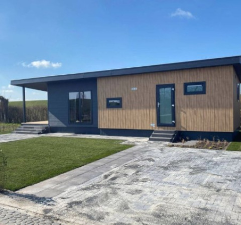 Moderne Lodge namens Dijkzicht mit Holzfassade und großen Fenstern, außen aufgenommen bei Sonnenschein.