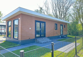Moderne lodge ved Parkzicht, Vakantiepark de Zeeuwse Parel i Nederlandene, omgivet af grønne træer.