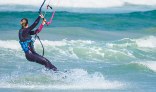 Persona haciendo kitesurf en el mar cerca de Vignole Mare SS, Cerdeña, Italia, con neopreno y chaleco.