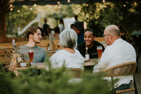 Cuatro personas charlan y disfrutan bebidas en una mesa al aire libre en Forest Lodge, Camping Si-Es-An, Países Bajos.