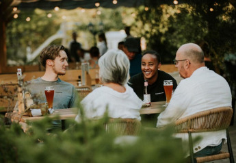 Cuatro personas charlan y disfrutan bebidas en una mesa al aire libre en Forest Lodge, Camping Si-Es-An, Países Bajos.