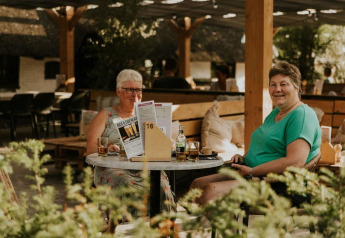 Dos mujeres disfrutan de una bebida en una mesa al aire libre en Forest Lodge, Camping Si-Es-An, Países Bajos.