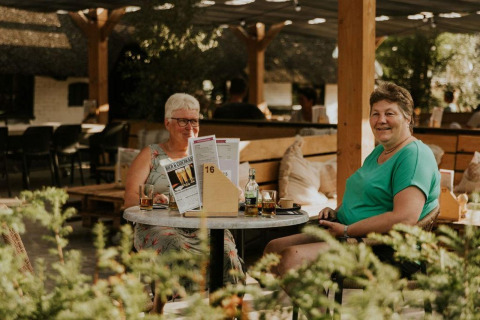 Zwei Frauen sitzen an einem Tisch und trinken im Freien in der Forest Lodge, Camping Si-Es-An, Niederlande.