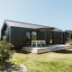 Sort trætinyhouse med terrasse på ferieparken De Klepperstee i Holland, udendørs siddeplads under parasol.