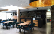 Moderne café og barområde med træborde og polstrede stole på Bospark De Brenkberg i Limburg, Holland.