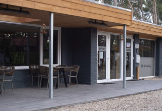 Eingang zum Ferienpark Bospark De Brenkberg in Limburg, Niederlande, mit Bistro und Außensitzplätzen.