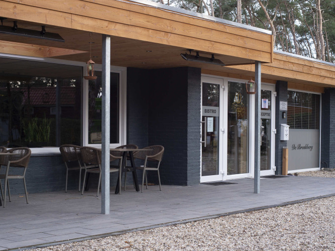 Entrance to Bospark De Brenkberg holiday park in Limburg, Netherlands with outdoor seating and wooded view.