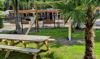 Red de escalada y mesa de picnic en Bospark De Brenkberg, un parque vacacional en Limburg, Países Bajos, rodeado de naturaleza.