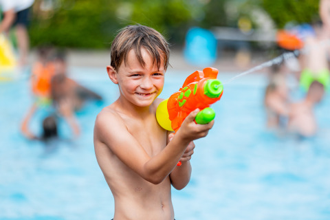 Junge spielt mit Wasserpistole am Pool im Vakantiepark Leukermeer, Ferienpark in Limburg, Niederlande.