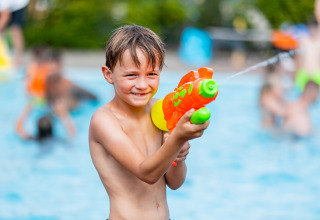Junge spielt mit Wasserpistole am Pool im Vakantiepark Leukermeer, Ferienpark in Limburg, Niederlande.