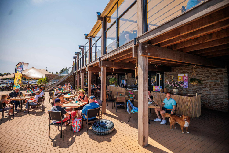Buitenterras van Vakantiepark Leukermeer met mensen en een hond die genieten van de zon in Limburg, Nederland.